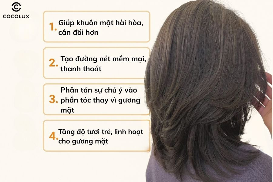 Một cô gái cười với mái tóc layer dài uốn sóng nhẹ, alt: Kiểu tóc layer dài uốn sóng nhẹ giúp gương mặt dài trông mềm mại, cân đối hơn